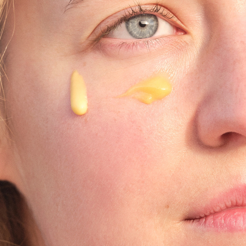 Close-up of a person's cheek with two dabs of jk7 cream applied below a light blue eye