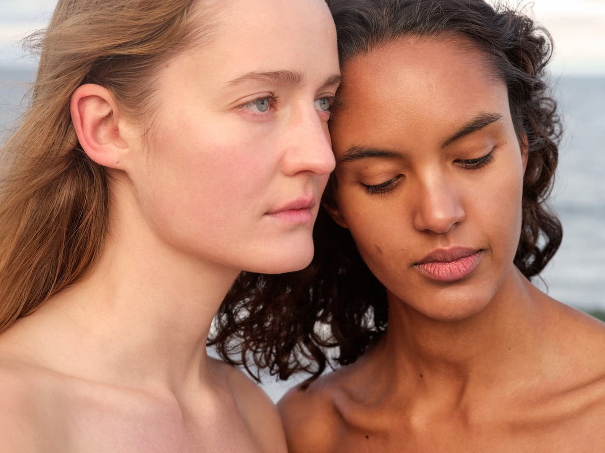 Two women with different skin type standing close together with a blurred natural background