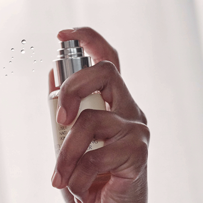A hand spraying a fine mist from a JK7 Beauty Moisturizing Mist against a bright, clean background.