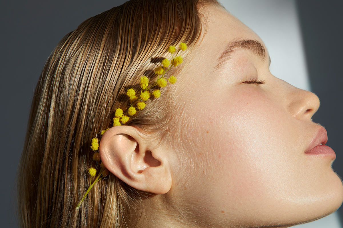 Close-up side profile of a woman with smooth skin and yellow mimosa flowers, symbolizing natural skin longevity and gentle aging.