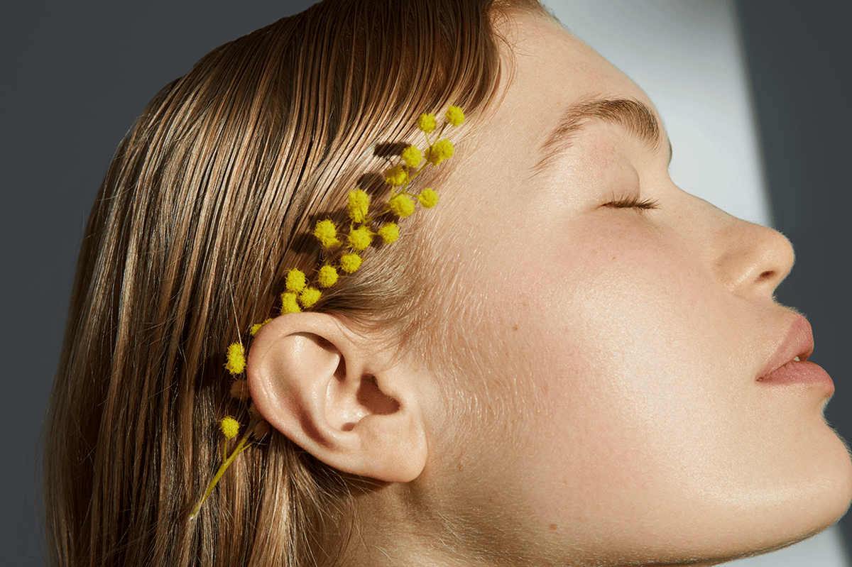 Close-up side profile of a woman with smooth skin and yellow mimosa flowers, symbolizing natural skin longevity and gentle aging.