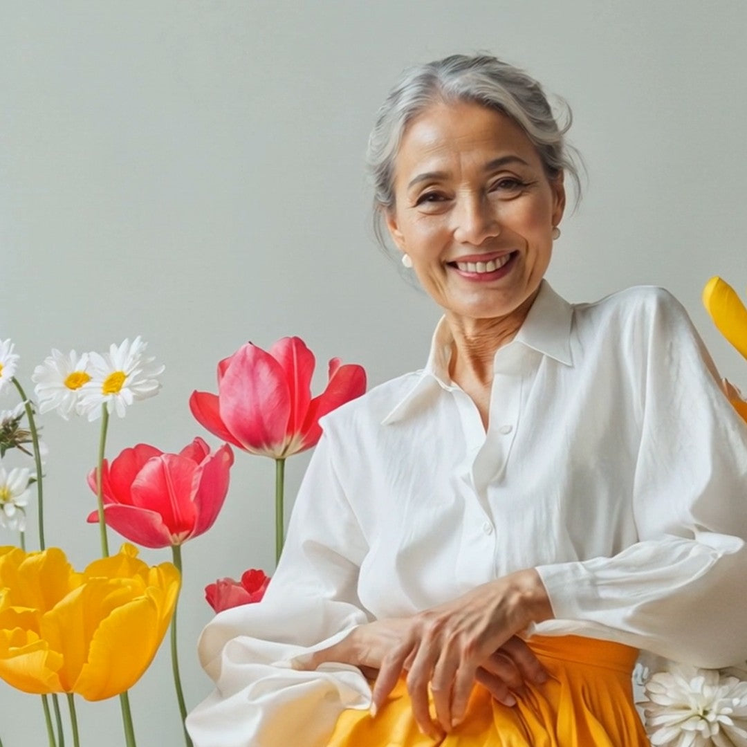 Confident mature woman seated in front of vibrant tulips and daisies, symbolizing healthy aging and long-term skin vitality.