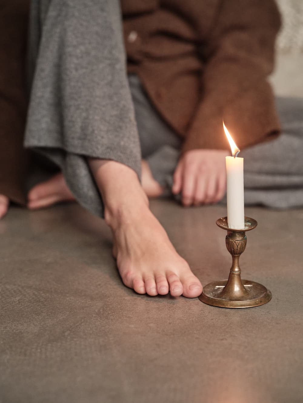 Person sitting on the floor with a lit candle in a brass holder