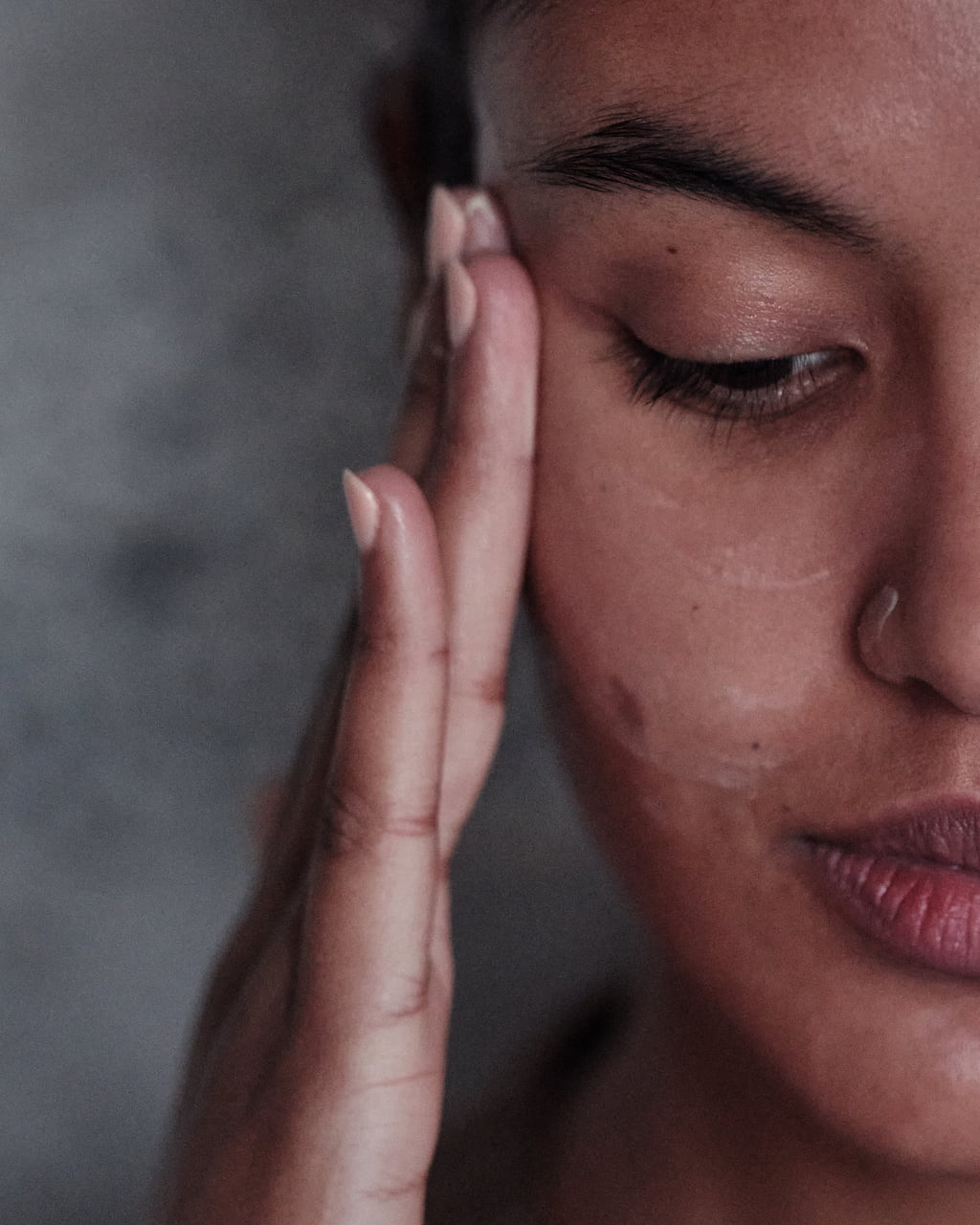 Close-up of a woman gently pressing skincare cream into her cheek with her fingertips.