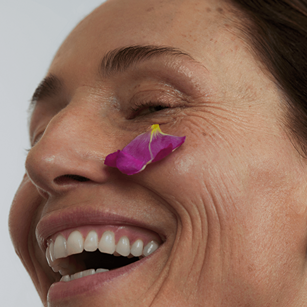 Smiling woman with a flower petal on her cheek, symbolising natural beauty and botanical skincare