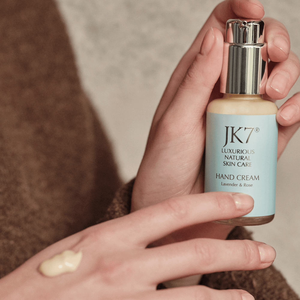 A hand holding a bottle of JK7 Hand Cream with a dollop of JK7 Hand Cream lavender and rose lotion on the back of the hand.